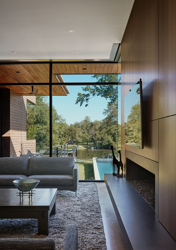 Стильный дизайн: большая парадная, открытая гостиная комната в стиле модернизм с коричневыми стенами, телевизором на стене, бетонным полом, горизонтальным камином, фасадом камина из дерева и серым полом - последний тренд