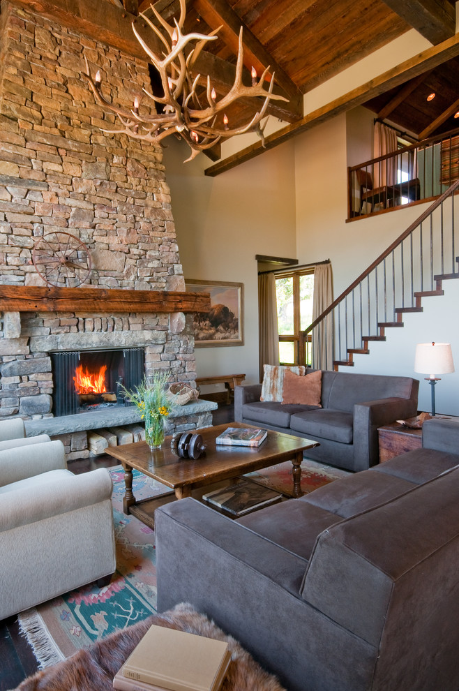 Пример оригинального дизайна: открытая гостиная комната в стиле рустика с стандартным камином, фасадом камина из камня, бежевыми стенами и коричневым диваном