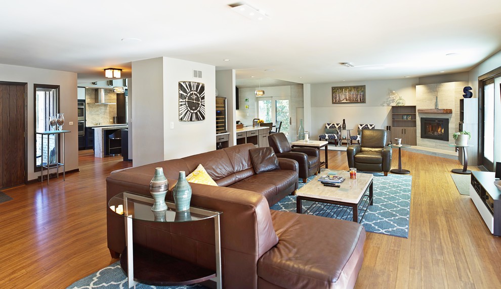 На фото: большая открытая гостиная комната в современном стиле с домашним баром, серыми стенами, полом из бамбука, угловым камином, фасадом камина из плитки и телевизором на стене с