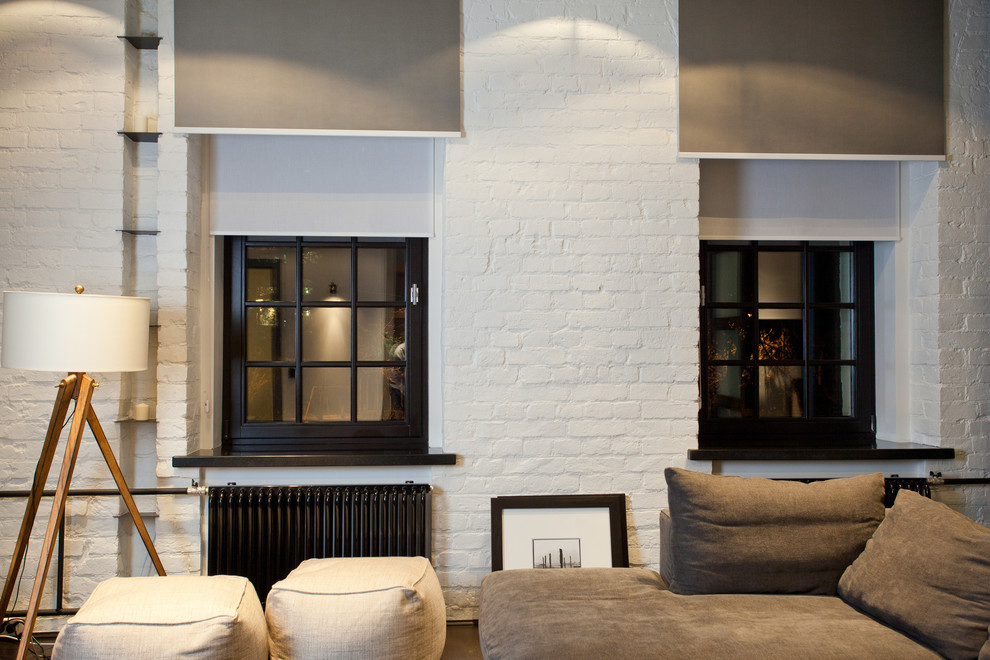 Imagen de salón abierto industrial pequeño con paredes blancas, suelo de madera oscura y televisor retractable