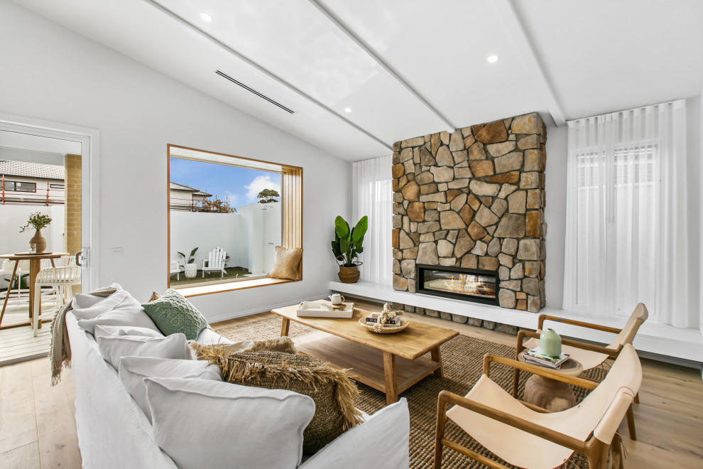 На фото: большая открытая гостиная комната в морском стиле с белыми стенами, стандартным камином и фасадом камина из камня