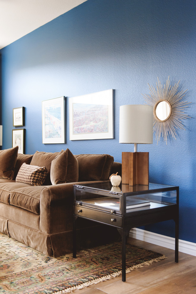 Foto di un piccolo soggiorno chiuso con pareti blu, pavimento in laminato, camino classico, cornice del camino in pietra ricostruita, TV a parete e pavimento marrone