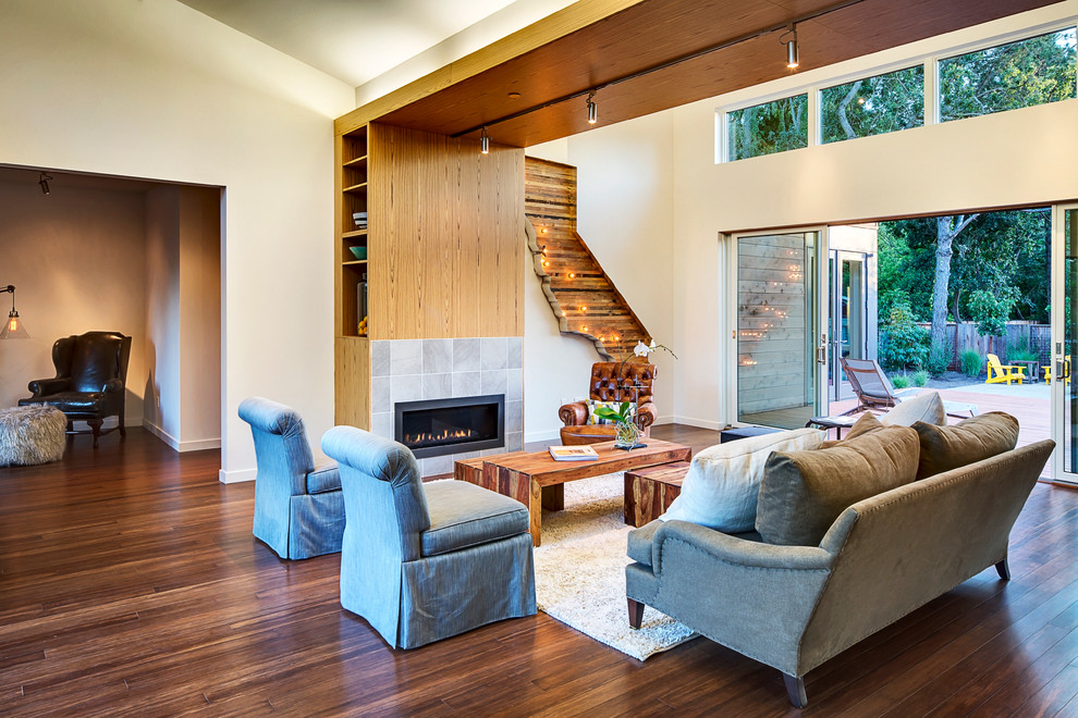 На фото: гостиная комната в современном стиле с фасадом камина из плитки, полом из бамбука, стандартным камином и ковром на полу с