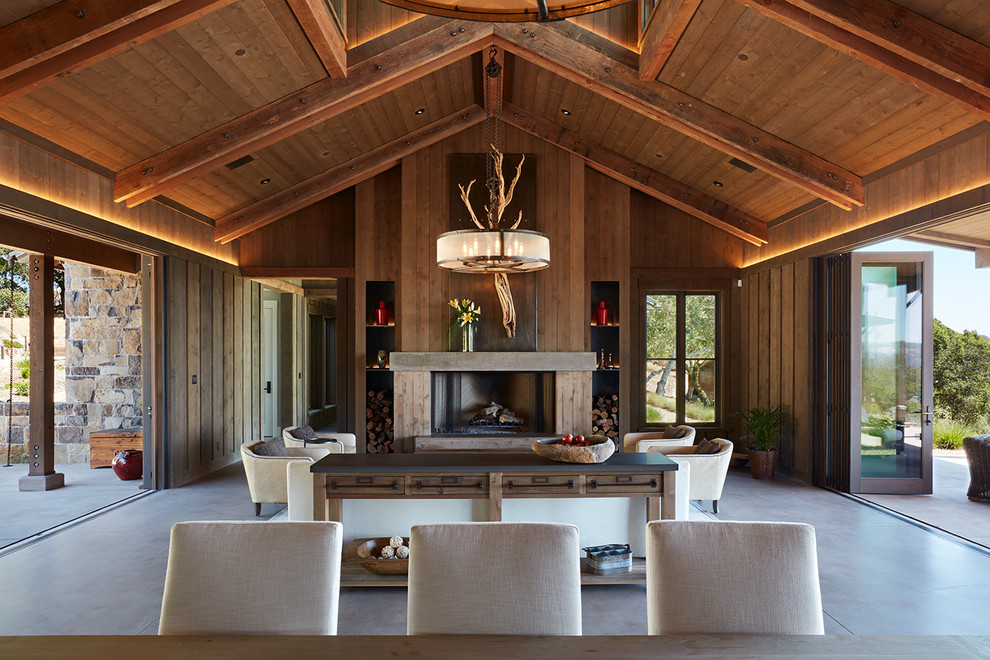 Foto de salón para visitas abierto de estilo de casa de campo con paredes marrones, suelo de cemento, chimenea lineal, marco de chimenea de madera y suelo gris