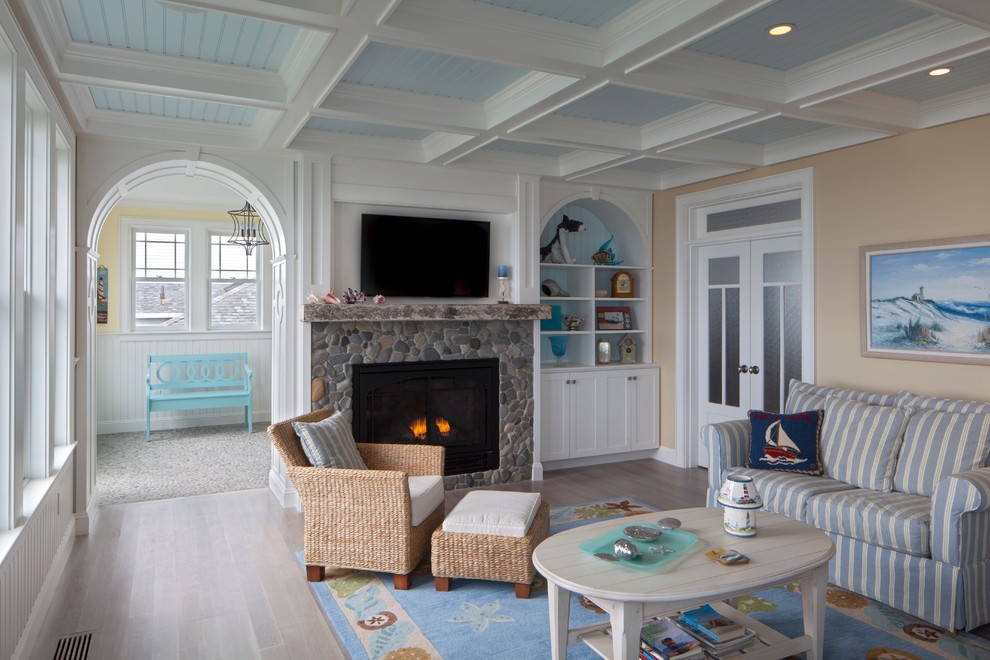 Foto de salón cerrado costero grande con suelo de madera clara, marco de chimenea de piedra y televisor colgado en la pared