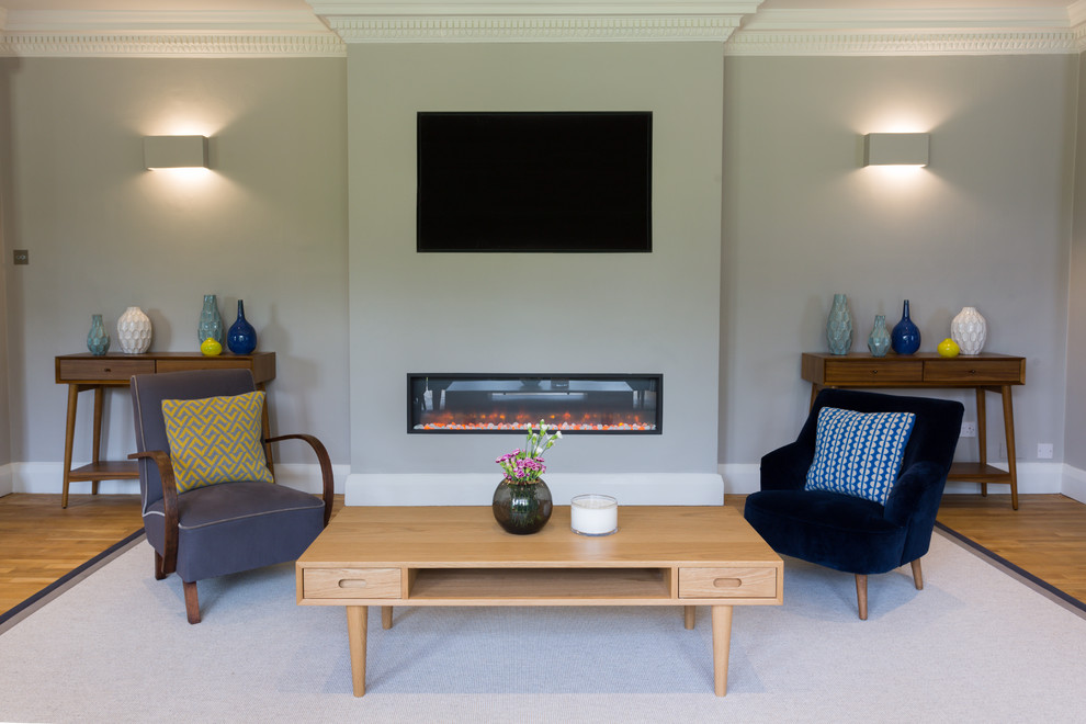 Imagen de salón cerrado vintage con paredes grises, suelo de madera clara, chimenea lineal y televisor colgado en la pared