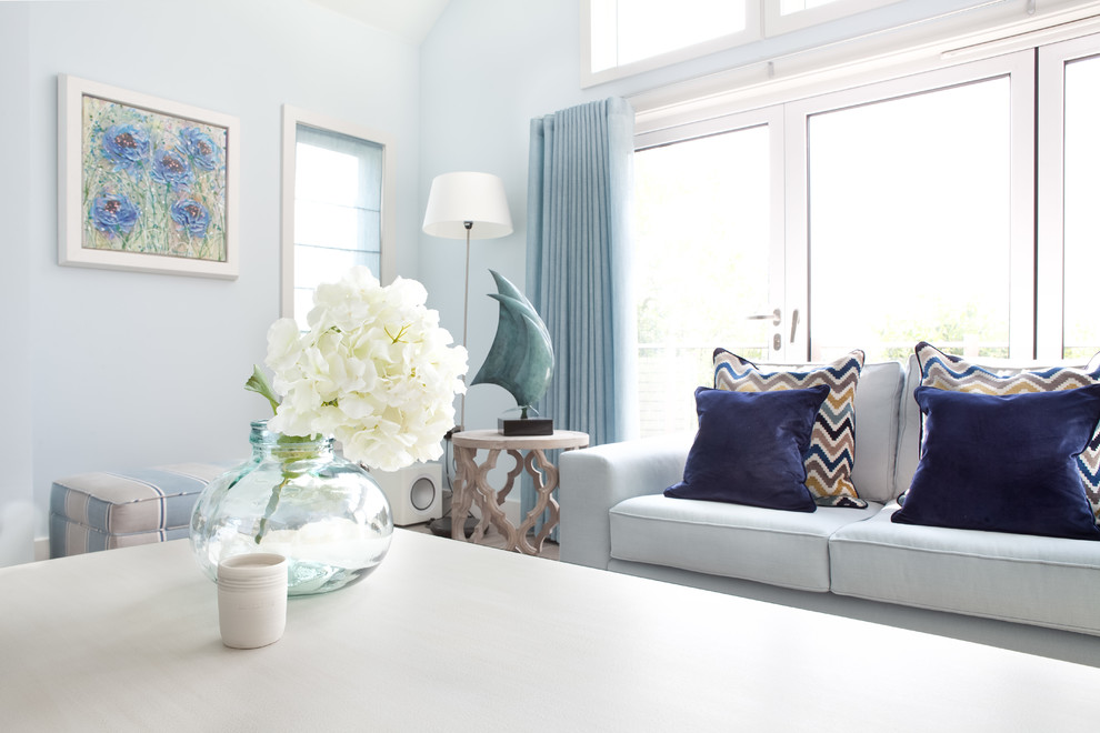 Aménagement d'un très grand salon bord de mer ouvert avec un mur bleu, parquet clair, une cheminée standard, un manteau de cheminée en plâtre, un téléviseur fixé au mur et un sol gris.