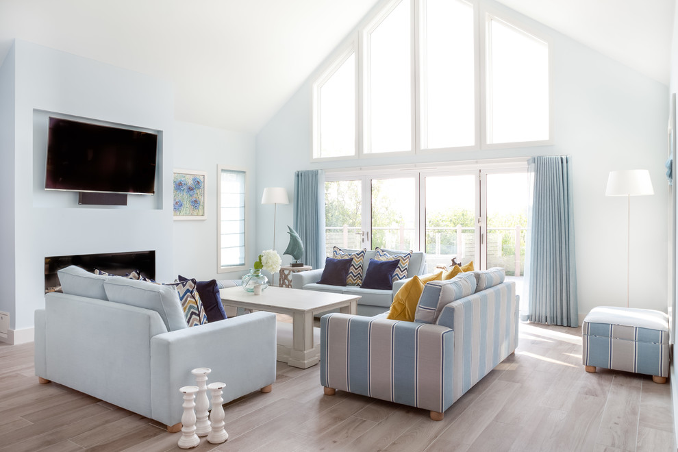 グロスタシャーにある高級な巨大なビーチスタイルのおしゃれなLDK (青い壁、淡色無垢フローリング、標準型暖炉、漆喰の暖炉まわり、壁掛け型テレビ、グレーの床) の写真