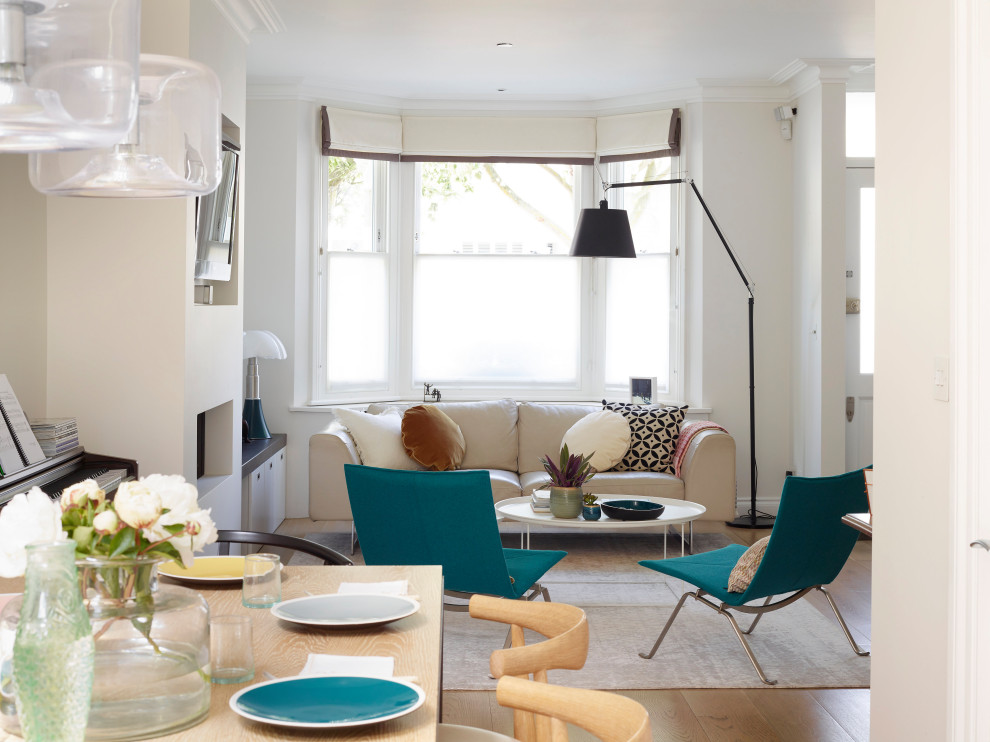 This is an example of a large contemporary formal open plan living room with beige walls, light hardwood flooring, a hanging fireplace, a plastered fireplace surround, a wall mounted tv and beige floors.