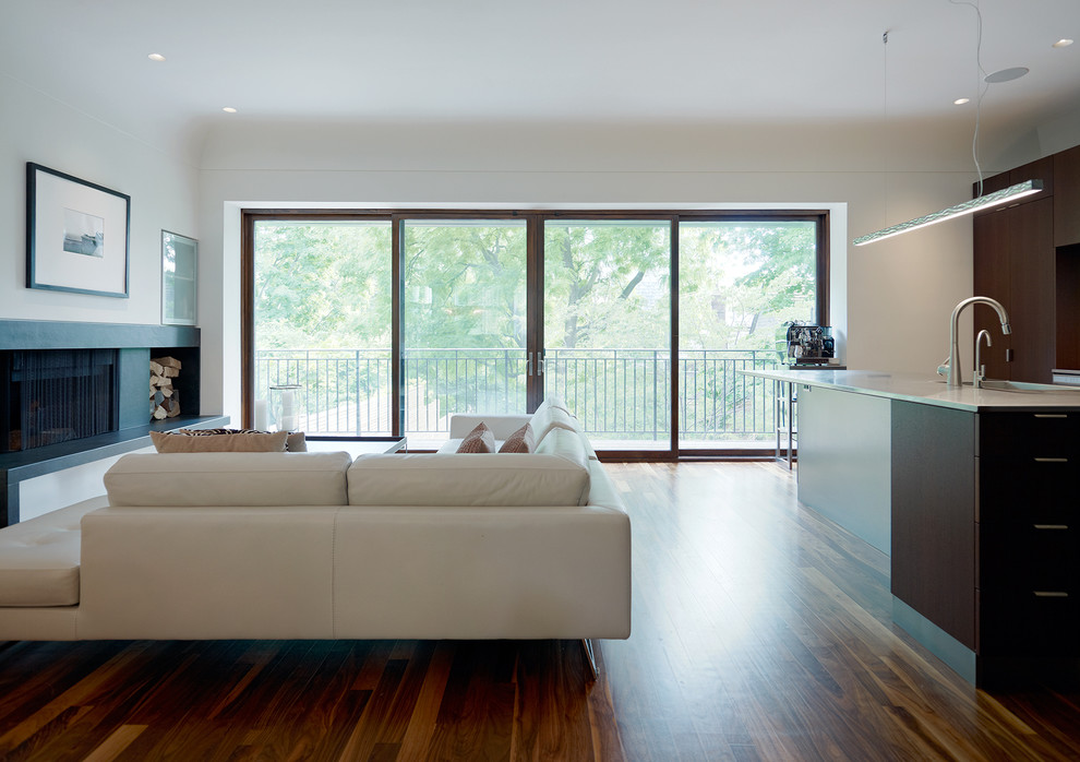 Modelo de salón para visitas abierto actual de tamaño medio con paredes blancas, suelo de madera en tonos medios, chimenea lineal y marco de chimenea de madera