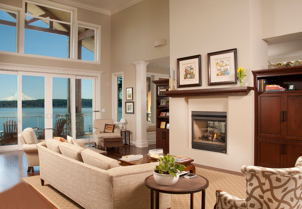 This is an example of a large traditional formal open plan living room in Seattle with beige walls, dark hardwood flooring, a two-sided fireplace, a stone fireplace surround and a concealed tv.