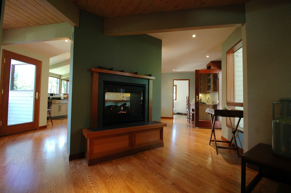 На фото: большая открытая гостиная комната в стиле ретро с зелеными стенами, паркетным полом среднего тона, двусторонним камином и фасадом камина из камня с