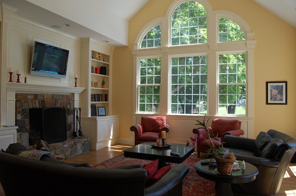 Пример оригинального дизайна: большая открытая гостиная комната в классическом стиле с желтыми стенами, паркетным полом среднего тона, стандартным камином, фасадом камина из камня, телевизором на стене и коричневым полом