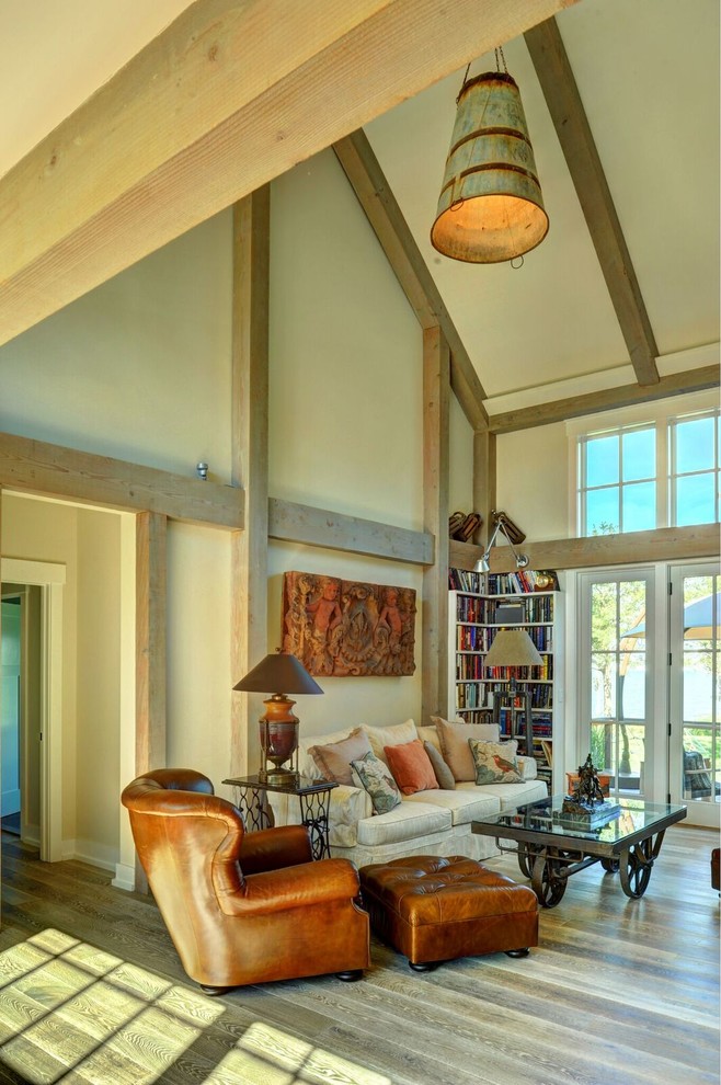 Diseño de salón abierto campestre grande con paredes beige, suelo de madera clara, chimenea de doble cara, marco de chimenea de ladrillo y televisor colgado en la pared