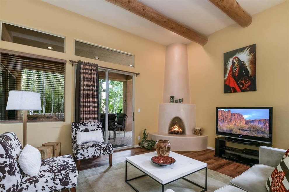 他の地域にある中くらいなサンタフェスタイルのおしゃれなLDK (黄色い壁、無垢フローリング、コーナー設置型暖炉、漆喰の暖炉まわり、据え置き型テレビ、茶色い床) の写真
