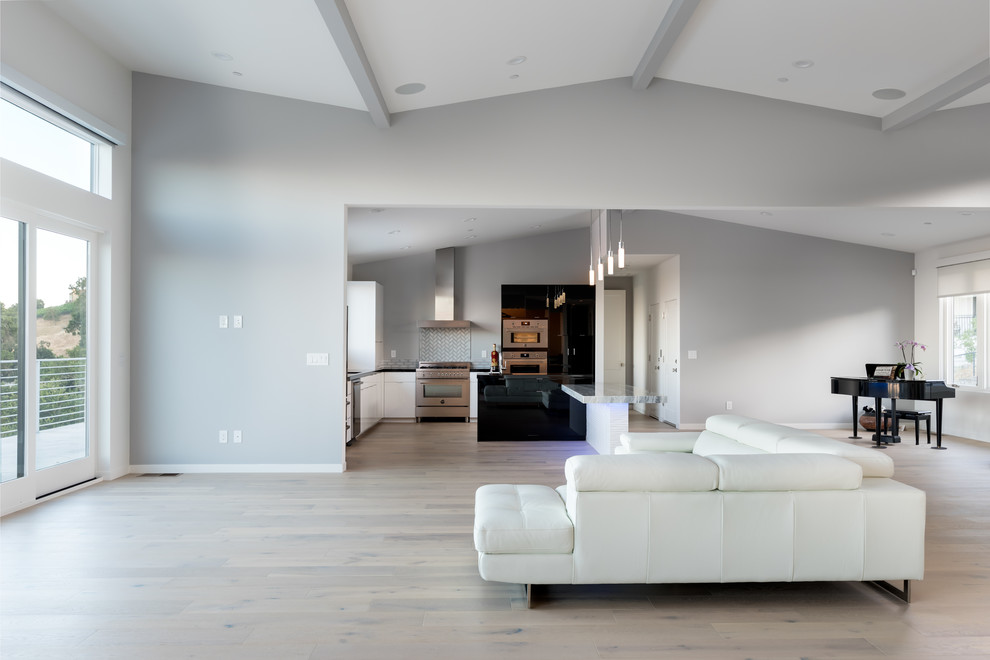 Ejemplo de salón para visitas abierto moderno grande sin chimenea y televisor con paredes grises, suelo de madera clara y suelo beige