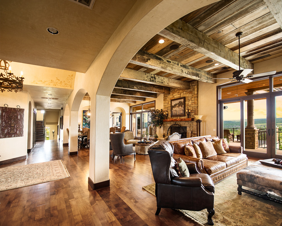 Offenes Mediterranes Wohnzimmer mit beiger Wandfarbe, braunem Holzboden, Kamin und Kaminumrandung aus Stein in Austin