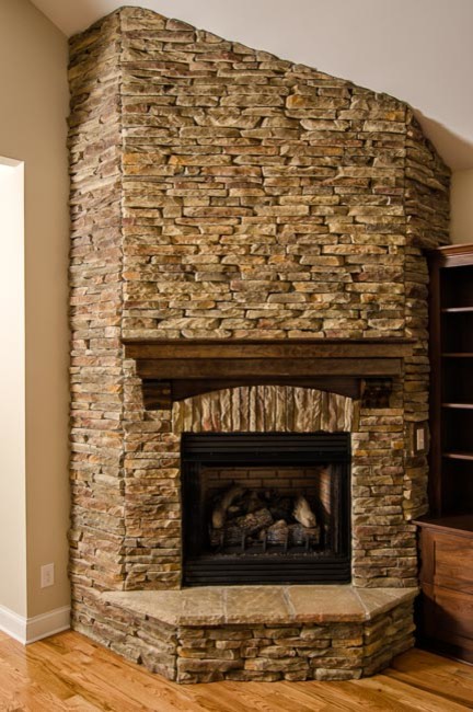 Cette photo montre un grand salon craftsman ouvert avec un mur beige, un sol en bois brun, une cheminée d'angle et un manteau de cheminée en pierre.