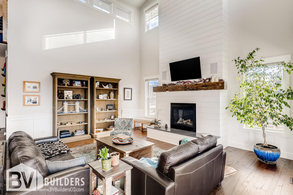 Offenes Landhaus Wohnzimmer mit braunem Holzboden, Kamin, Kaminumrandung aus Holzdielen, TV-Wand, braunem Boden und vertäfelten Wänden in Denver