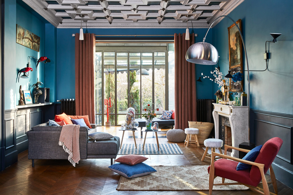 Modelo de salón bohemio con paredes azules, suelo de madera en tonos medios, todas las chimeneas y suelo marrón