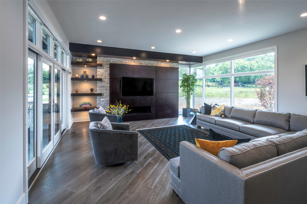 Diseño de salón abierto minimalista grande con paredes grises, suelo de madera clara, chimenea lineal, marco de chimenea de madera y televisor colgado en la pared