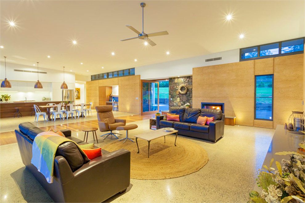 Источник вдохновения для домашнего уюта: огромная открытая гостиная комната в современном стиле с бежевыми стенами, бетонным полом, стандартным камином, фасадом камина из камня и телевизором на стене