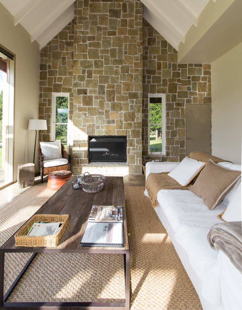 Ejemplo de salón abierto campestre de tamaño medio sin televisor con paredes beige, todas las chimeneas, marco de chimenea de piedra y suelo de cemento