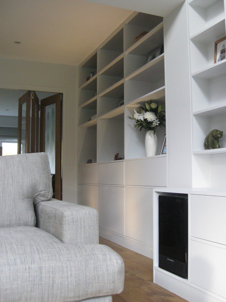 Cette image montre un salon design avec un mur blanc, un sol en bois brun et un téléviseur encastré.