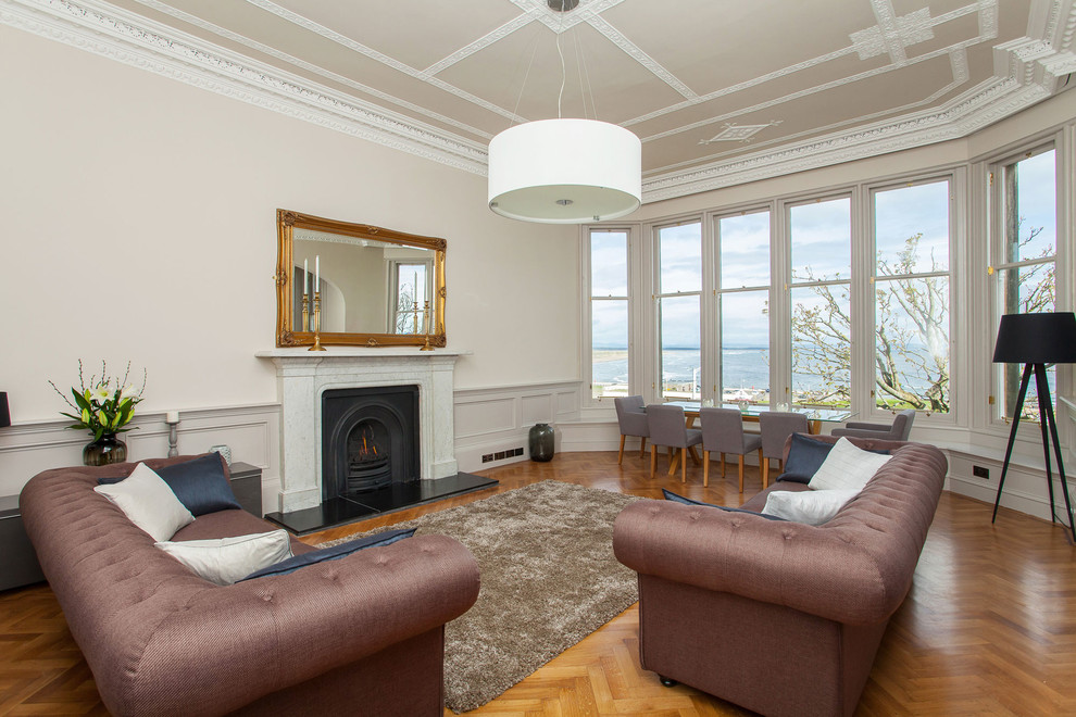 Пример оригинального дизайна: гостиная комната в классическом стиле с бежевыми стенами, паркетным полом среднего тона, стандартным камином и коричневым диваном