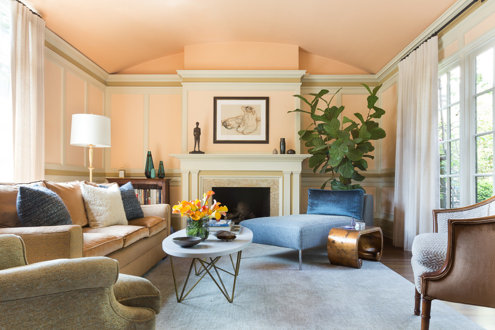 Пример оригинального дизайна: парадная гостиная комната в стиле неоклассика (современная классика) с оранжевыми стенами, темным паркетным полом и стандартным камином без телевизора