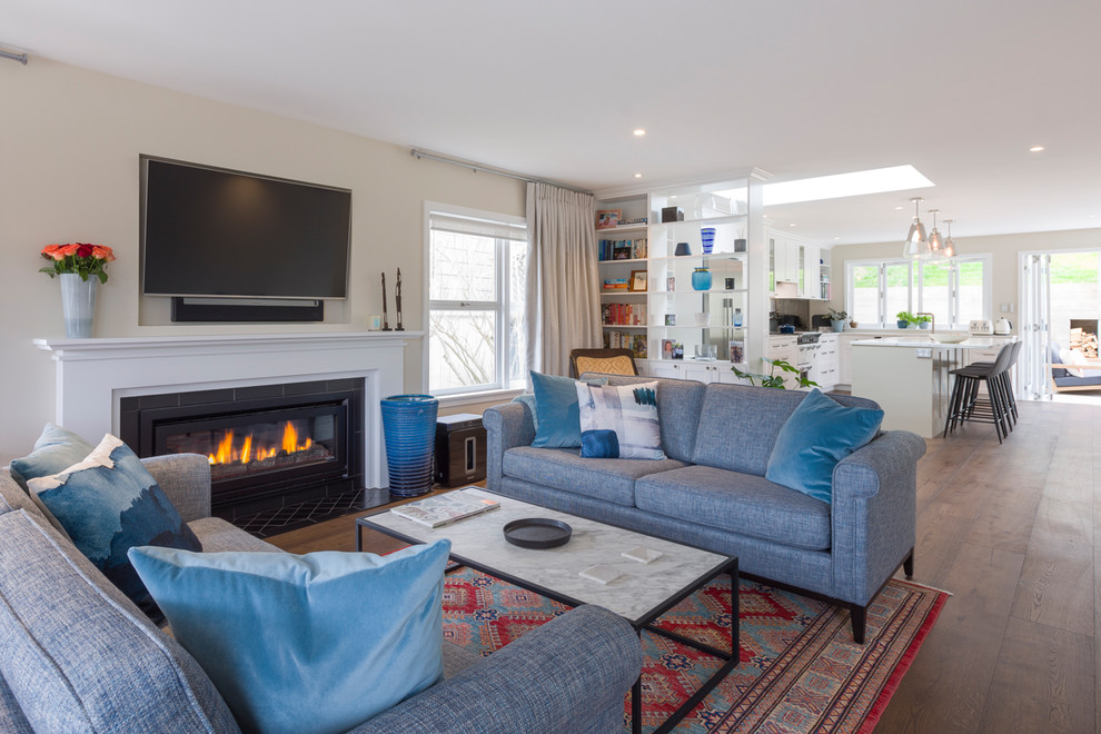 Inspiration for a large contemporary open concept medium tone wood floor and brown floor living room remodel in Auckland with beige walls, a standard fireplace, a plaster fireplace and a wall-mounted tv