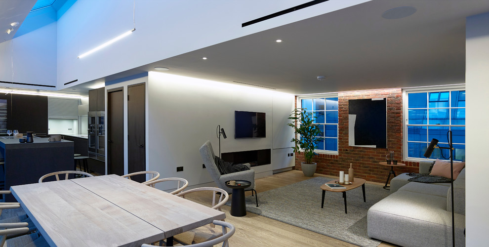 Foto de salón abierto contemporáneo de tamaño medio con paredes grises, suelo de madera clara, chimenea lineal, marco de chimenea de metal y televisor colgado en la pared