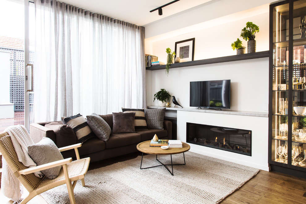 Стильный дизайн: гостиная комната в современном стиле с белыми стенами, паркетным полом среднего тона, горизонтальным камином, отдельно стоящим телевизором и коричневым полом - последний тренд