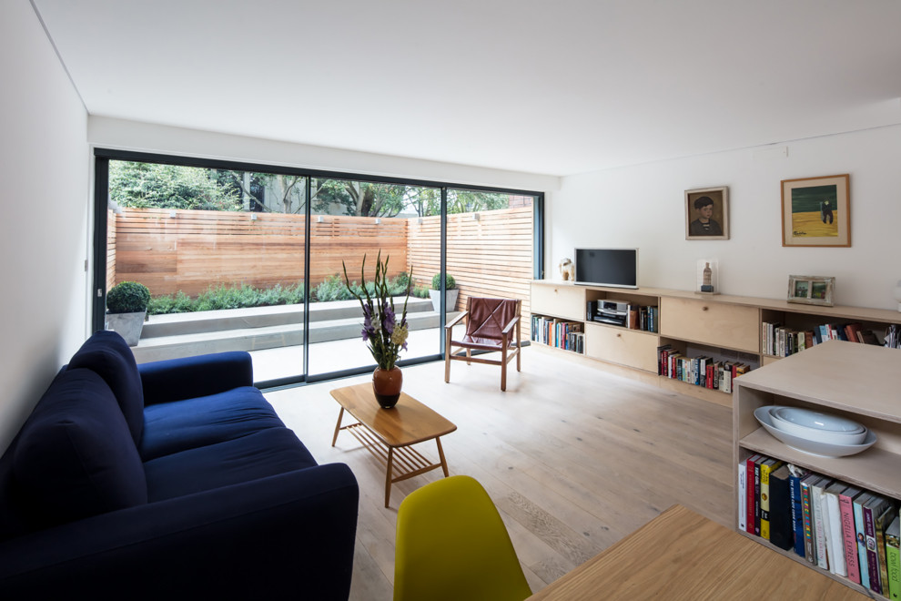 Modelo de biblioteca en casa abierta actual grande sin televisor con paredes blancas, suelo de madera clara y suelo beige