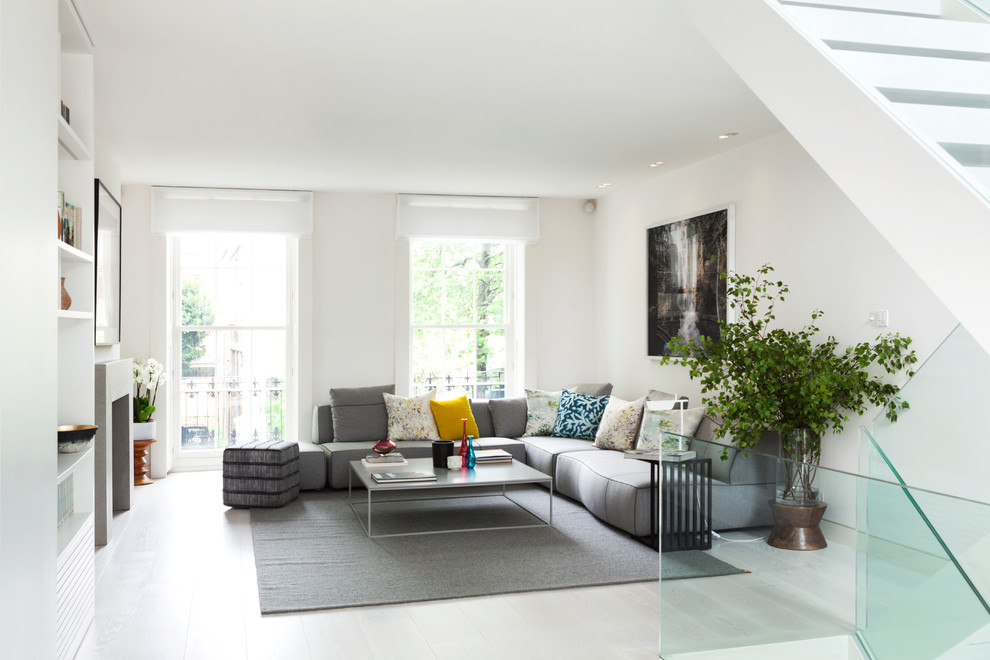 This is an example of a medium sized contemporary formal open plan living room in London with white walls, light hardwood flooring, a standard fireplace, a stone fireplace surround and no tv.