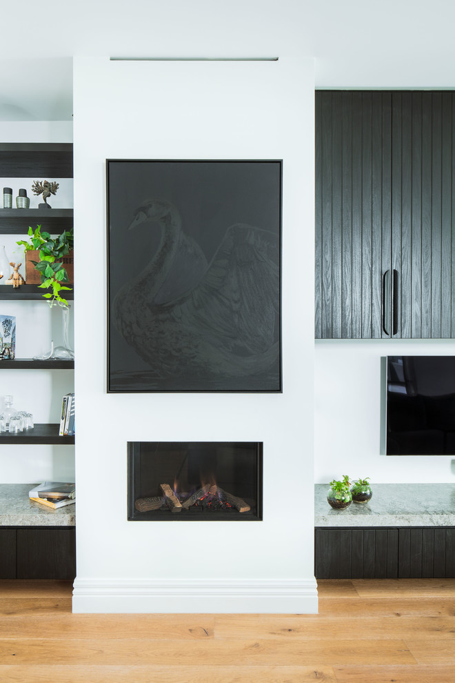 Imagen de salón para visitas abierto actual de tamaño medio con paredes negras, suelo de madera clara, estufa de leña, marco de chimenea de yeso y pared multimedia