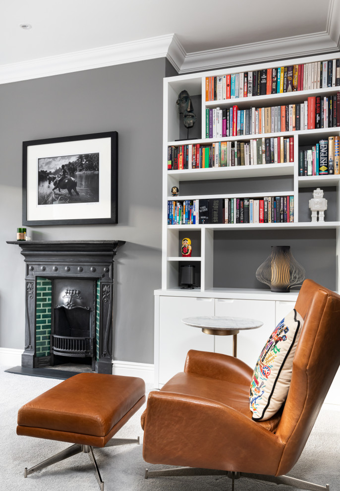 Cette photo montre un grand salon chic fermé avec une bibliothèque ou un coin lecture, un mur gris, moquette, une cheminée standard, un manteau de cheminée en pierre, un téléviseur indépendant et un sol gris.
