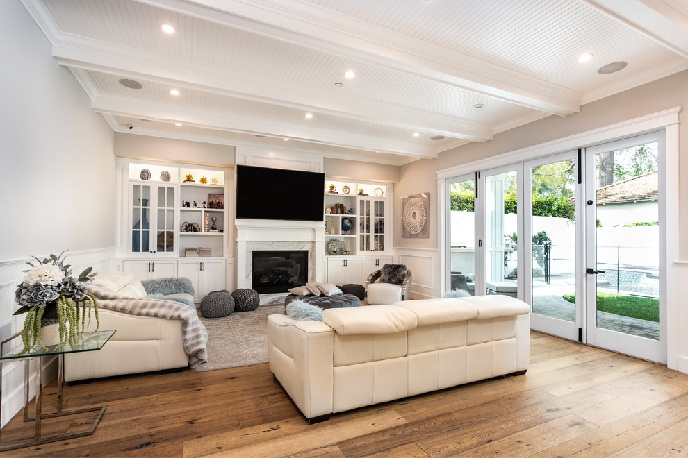 Klassisches Wohnzimmer mit beiger Wandfarbe, braunem Holzboden, Kamin, TV-Wand und braunem Boden in Los Angeles