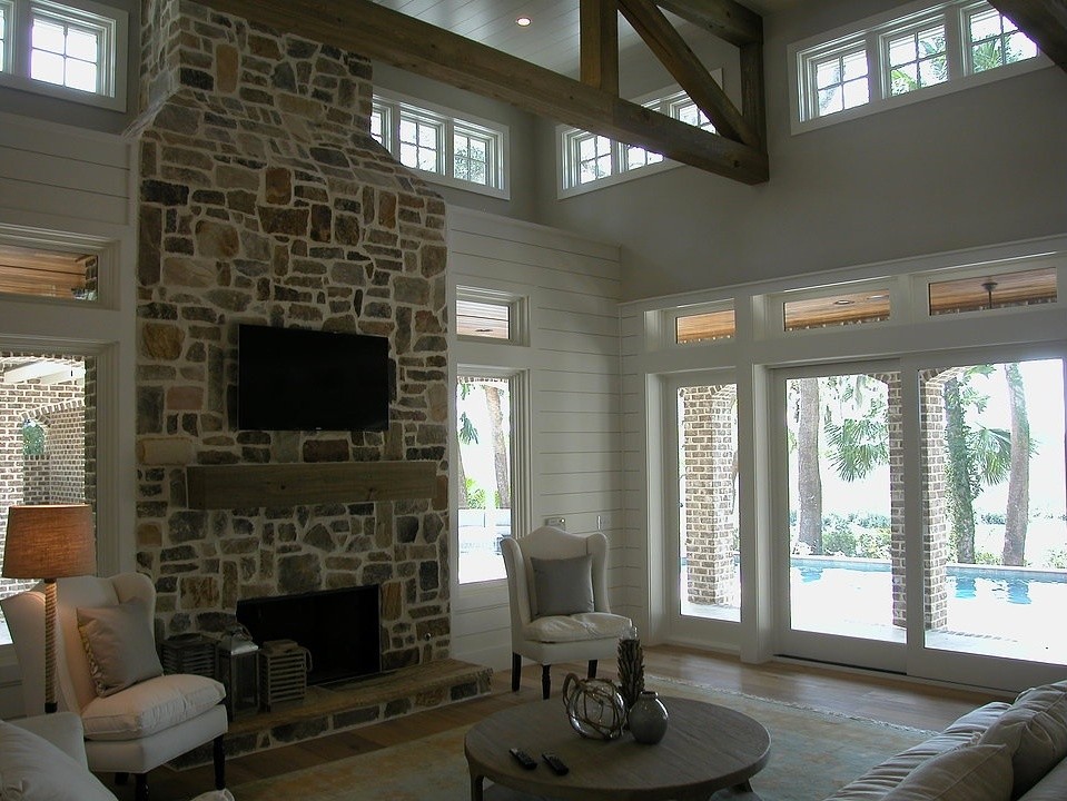 На фото: большая открытая гостиная комната в классическом стиле с белыми стенами, паркетным полом среднего тона, стандартным камином, фасадом камина из камня, телевизором на стене и коричневым полом