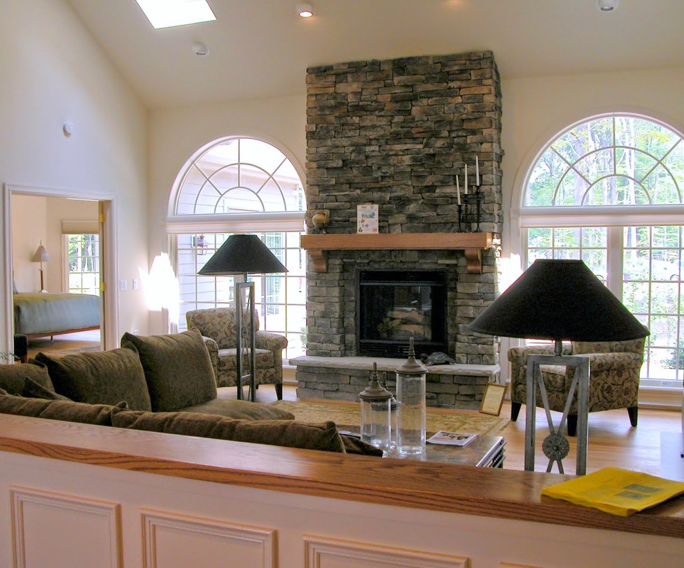 Cette image montre un grand salon traditionnel ouvert avec une salle de réception, un mur blanc, un sol en bois brun, une cheminée standard, un manteau de cheminée en pierre et un téléviseur indépendant.