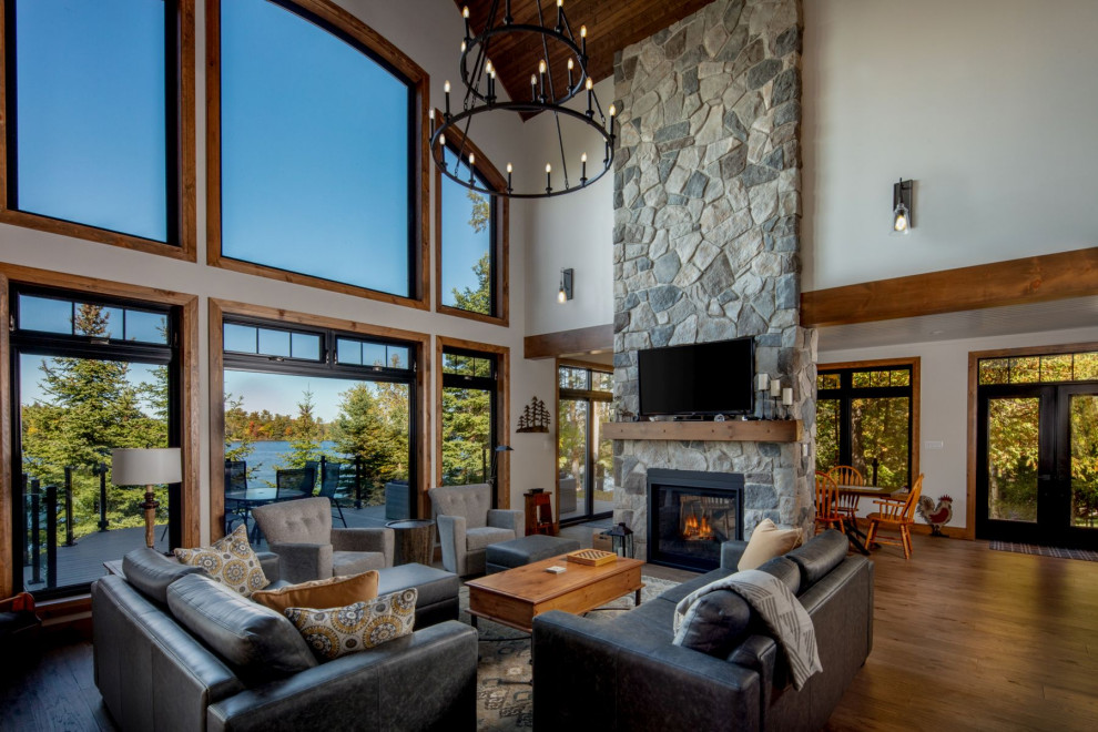 Mountain style open concept medium tone wood floor, brown floor, vaulted ceiling and wood ceiling living room photo in Toronto with white walls, a two-sided fireplace, a stone fireplace and a wall-mounted tv