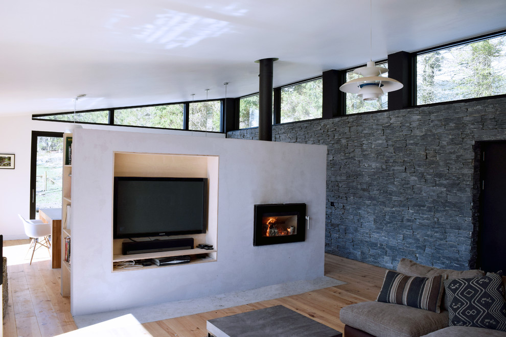 Aménagement d'un salon contemporain de taille moyenne et ouvert avec un mur gris, parquet clair, un poêle à bois, un manteau de cheminée en béton et un téléviseur encastré.