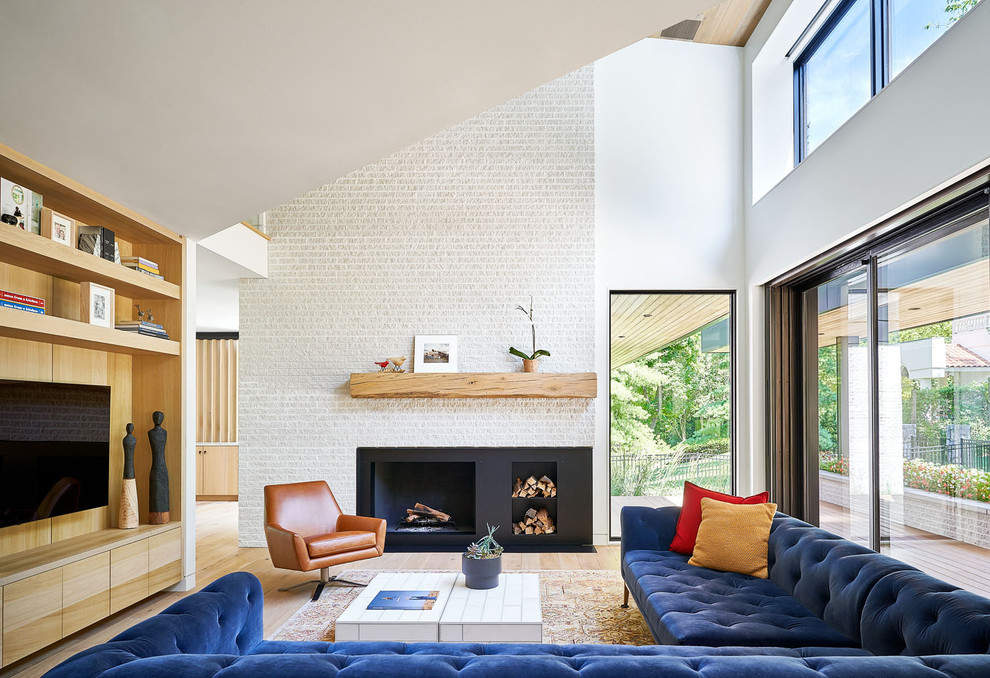 This is an example of a contemporary open plan living room in Kansas City with white walls, light hardwood flooring, a standard fireplace, a wall mounted tv and brown floors.