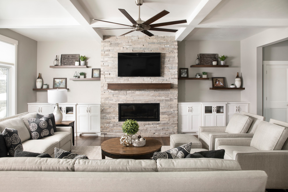 Пример оригинального дизайна: открытая гостиная комната среднего размера в стиле неоклассика (современная классика) с серыми стенами, темным паркетным полом, стандартным камином, фасадом камина из камня, телевизором на стене и коричневым полом