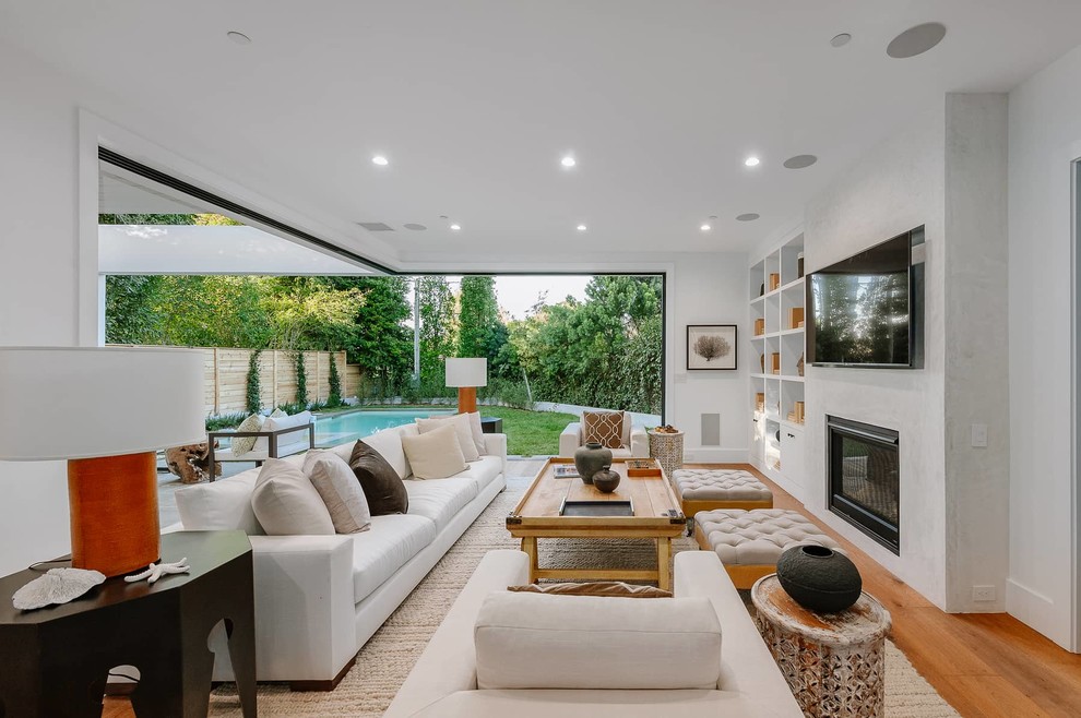 Großes, Offenes Landhaus Wohnzimmer mit weißer Wandfarbe, braunem Holzboden, Kamin und braunem Boden in Los Angeles