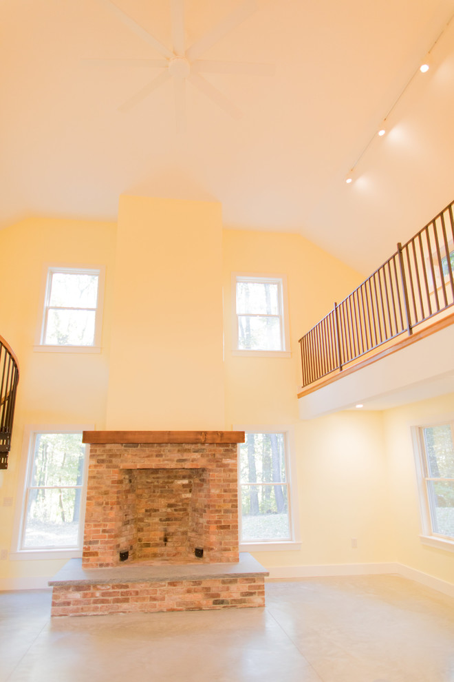 Geräumiges, Offenes Mediterranes Wohnzimmer mit gelber Wandfarbe, Betonboden, Kamin, Kaminumrandung aus Backstein und grauem Boden in Boston
