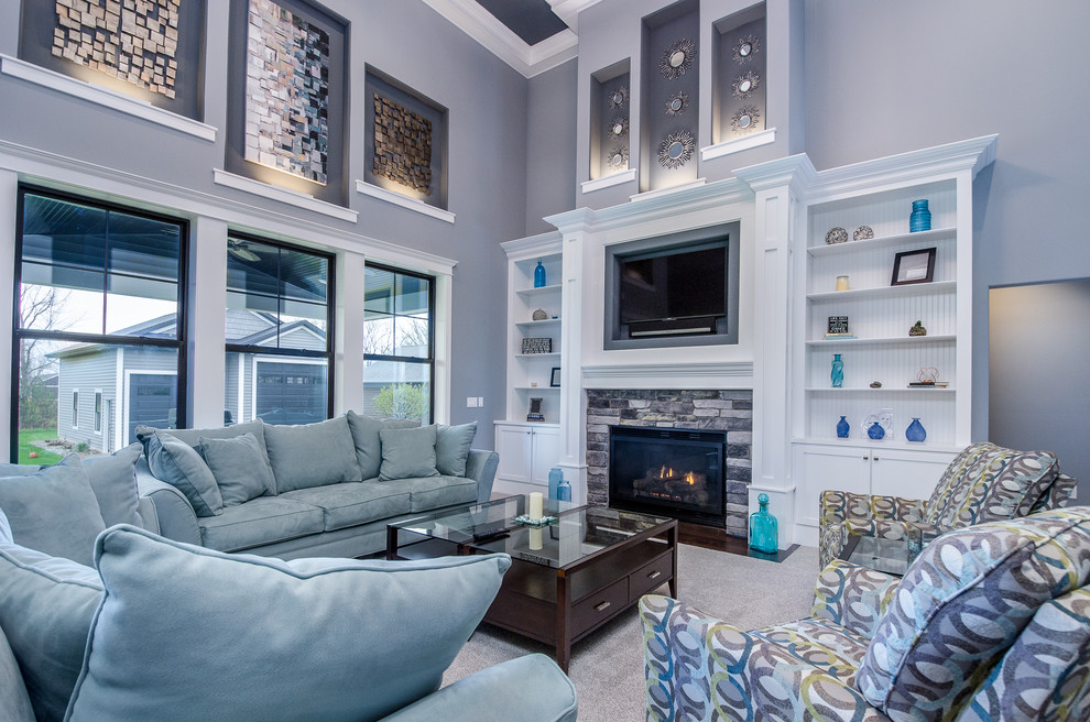 Источник вдохновения для домашнего уюта: гостиная комната в стиле неоклассика (современная классика) с серыми стенами, ковровым покрытием, стандартным камином, фасадом камина из камня, телевизором на стене, бежевым полом и синим диваном