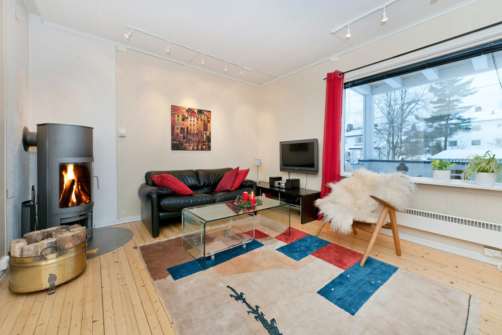 Mittelgroßes, Abgetrenntes Modernes Wohnzimmer mit beiger Wandfarbe, hellem Holzboden, Kaminofen, Kaminumrandung aus Beton und TV-Wand in Sonstige