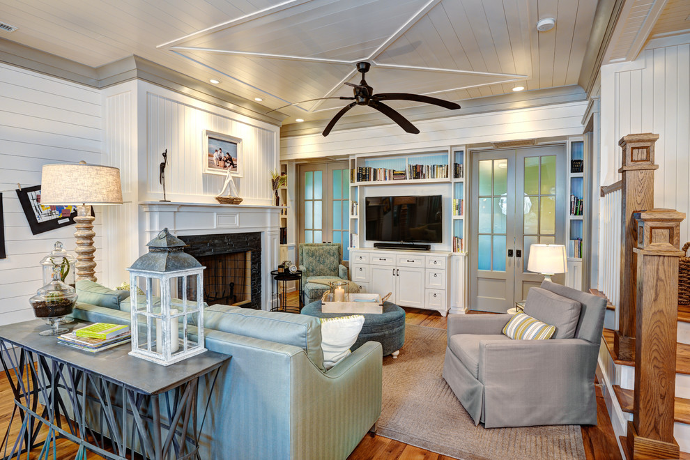 Mittelgroßes, Offenes Maritimes Wohnzimmer mit weißer Wandfarbe, braunem Holzboden, Kamin, Kaminumrandung aus Stein und freistehendem TV in Charleston