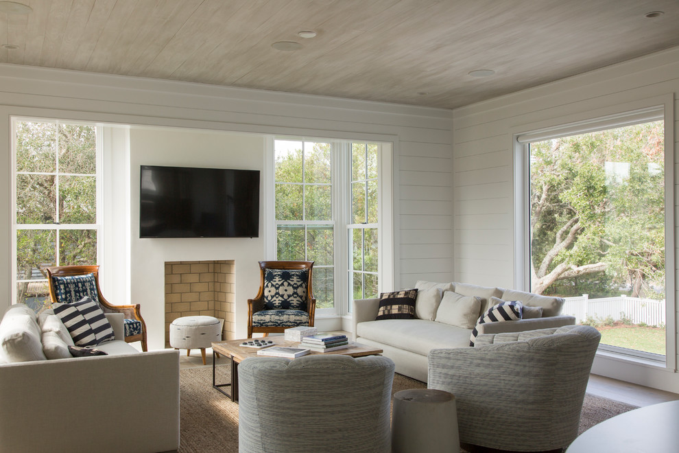 Diseño de salón abierto costero con paredes blancas, suelo de madera clara, todas las chimeneas, marco de chimenea de yeso y televisor colgado en la pared